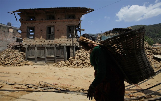 A Nepalese woman carries a basket and walks past a damaged house in Kathmandu, Nepal, Saturday, May 2, 2015.