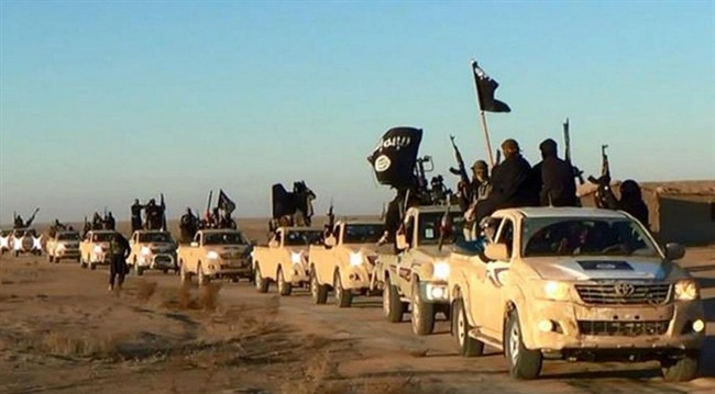 In this undated file photo, militants of the Islamic State group hold up their weapons and wave its flags on their vehicles in a convoy on a road leading to Iraq, while riding in Raqqa city in Syria.