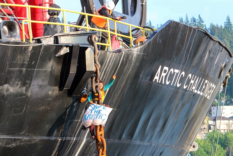  this Friday, May 22, 2015 photo provided by Reese Semanko, a woman identified as Chiara Rose has suspended herself in a climbing harness from the anchor chain of the Royal Dutch Shell support ship Arctic Challenger in the harbor at Bellingham, Wash. Rob Lewis, spokesman for protest organizers Rising Tide Bellingham, said Lewis said she is protesting Shell's plan for Arctic drilling. The Coast Guard says it has no plans to remove her but has impounded the activists' support vessels. The ship isn't scheduled to leave the port for several days.