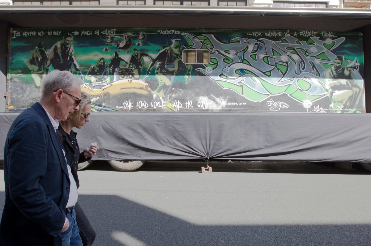 In this photo taken Saturday May 30, 2015, people walk past a trailer which British street artist Banksy turned into a piece entitled "Silent Majority", as it is displayed outside the Digard auction house in Paris. 