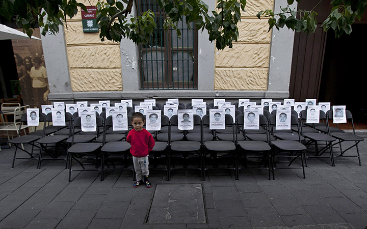 A child stands before a memorial made up of empty chairs bearing images of the 43 missing students, to mark the nine-month anniversary of their disappearance, in Mexico City, Saturday, June 27, 2015.