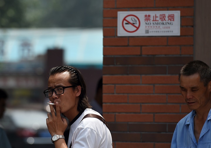 A man smokes a cigarette near a new no-smoking sign at the entrance to a childrens hospital in Beijing on June 1, 2015.