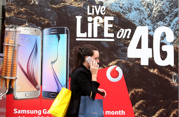 A pedestrian talks on her mobile phone device as she walks past a Vodafone advertisement outside a store, operated by Vodafone Group Plc, in London, U.K., on Friday, June 5, 2015.