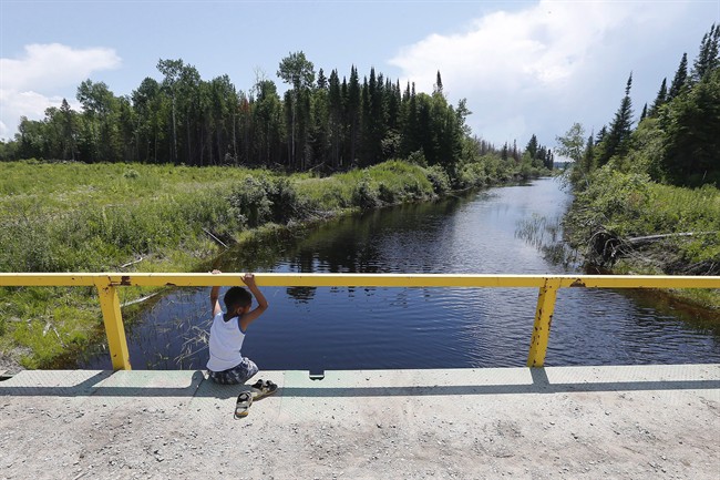A boy from the Shoal Lake 40 First Nation sits on a bridge over a channel on on Thursday, June 25, 2015. crowdfunding campaign is underway to pay Ottawa's portion of an all-weather road for a reserve under one of the longest boil-water advisories in Canada.