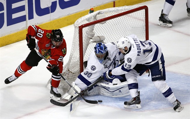 Chicago Blackhawks' Brandon Saad, left, reaches for a puck as Tampa Bay Lightning goalie Ben Bishop and Cedric Paquette, right, defend during the third period in Game 3 of the NHL hockey Stanley Cup Final on Monday, June 8, 2015, in Chicago.