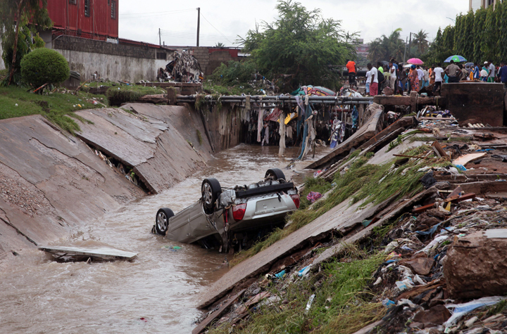 A car lies in a water trench that washed away after heavy rain near a gas station explosion in Accra, Ghana, Thursday, June 4, 2015. Flooding in Ghana’s capital swept stored fuel into a nearby fire, setting off a huge explosion at a gas station that killed scores of people and set alight neighboring buildings, authorities said Thursday.