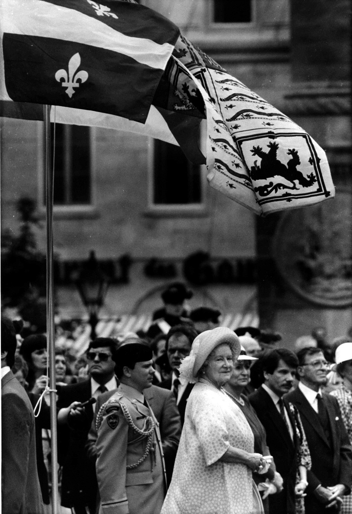 The Queen Mother takes the salute from the Black Watch of Canada as the Quebec and Black Watch flags fly overhead in Montreal, Quebec June 4, 1987. Standing to the left of her Majesty are Mayor Jean Dore and his wife, and Lt. Governor of Quebec, Gilles Lamontagne.