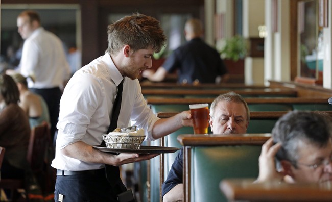 FILE - In this May 14, 2014, file photo, waiter Spencer Meline serves a customer at Ivar's Acres of Clams restaurant on the Seattle waterfront. Two new reports examining the impact of a minimum wage increase in the city delivered conflicting results.