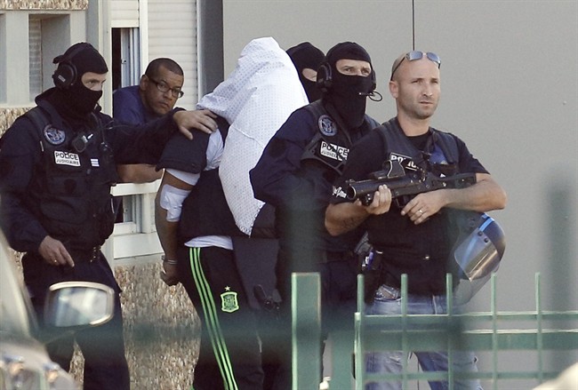 The suspect in the beheading of a businessman, Yassine Salhi, a towel over his head to mask his face, is escorted by police officers as they leave his home in Saint-Priest, outside the city of Lyon, central France, Sunday, June 28, 2015.