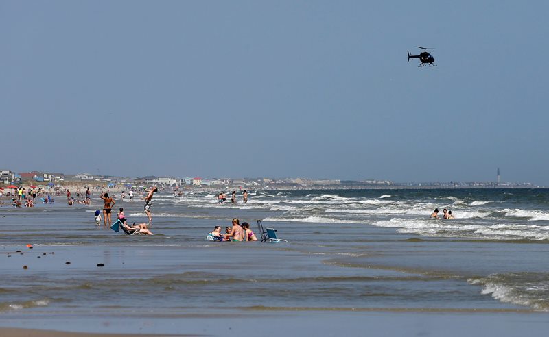 A helicopter flies close to the water as vacationers relax on the beach in Oak Island, N.C., Monday, June 15, 2015. A 12-year-old girl from Asheboro lost part of her arm and suffered a leg injury, and a 16-year-old boy from Colorado lost his left arm about an hour later and 2 miles away in two separate shark attacks late Sunday afternoon. 