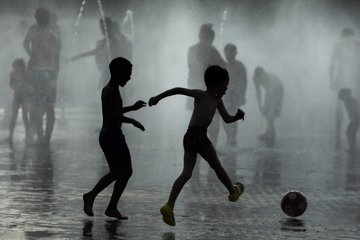 Children play soccer as they cool down in a fountain beside Manzanares river in Madrid, Spain, Monday, June 29, 2015. 