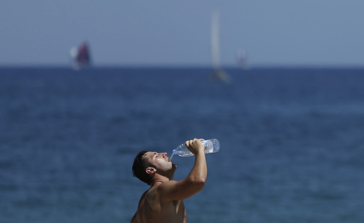 A man drinks water on a beach in Barcelona, Spain, Sunday, June 28, 2015. Weather stations across Spain are warning people to take extra precautions as a heat wave engulfs much of the country.