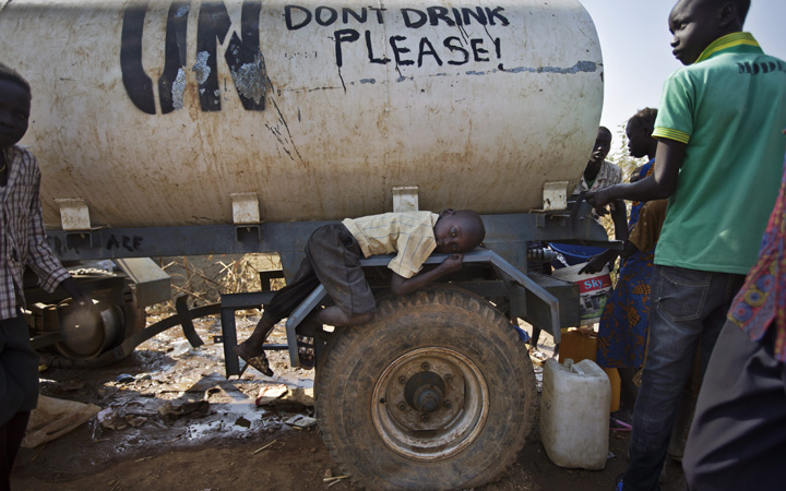 A young displaced boy rests on the wheel arch of a water truck while others fill containers from it, at a United Nations compound which has become home to thousands of people displaced by the recent fighting, in the Jebel area on the outskirts of Juba, South Sudan.