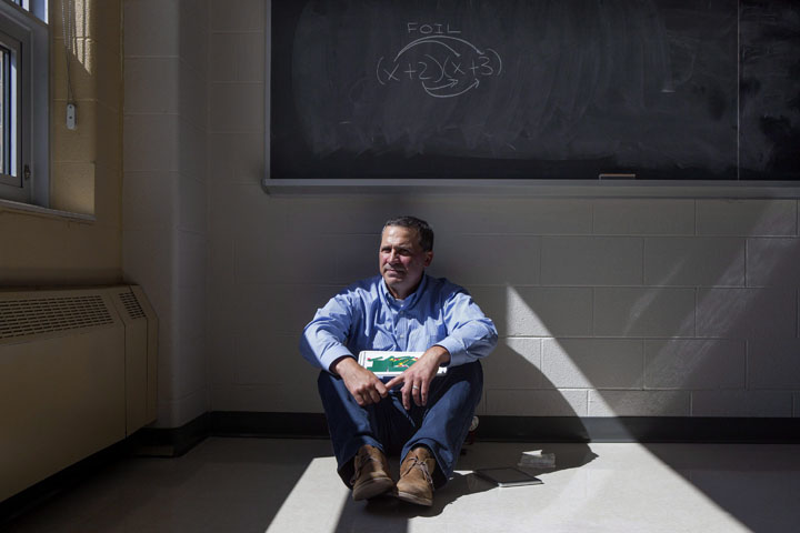 Math teacher Paul Alves holds a visual learning aid as he sits below a traditional math equation on a classroom's chalk board at Fletcher's Meadow Secondary School in Brampton, Ont., on Wednesday, June 24, 2015. 