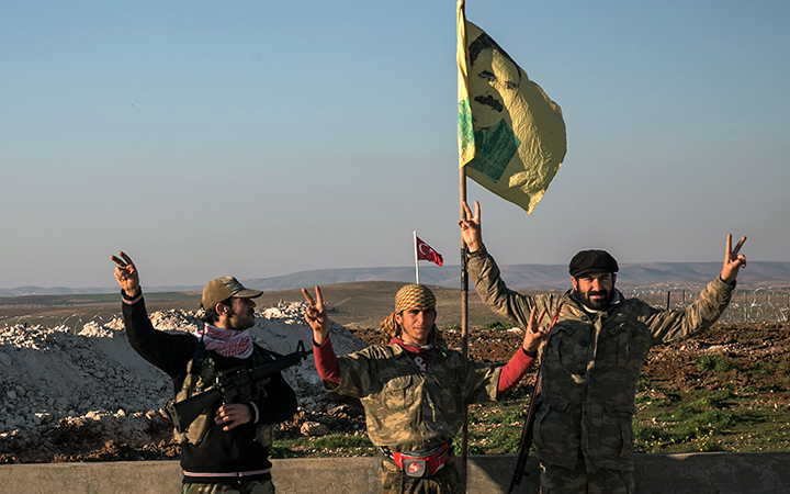 Syrian Kurdish militia members of YPG make a V-sign next to poster of Abdullah Ocalan, jailed Kurdish rebel leader, and a Turkish army tank in the background in Esme village in Aleppo province, Syria on Feb. 22, 2015. 
