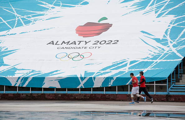 Runners jog past an advertisement for "Almaty 2022," candidate city for the Winter Olympics, as they train at the Medeo sports stadium in Almaty, Kazakhstan, on Saturday, June 27, 2015. Almaty, with a population of 1.6 million in the foothills of the Tian Shan mountains, is bidding to host the 2022 Winter Olympic games. 