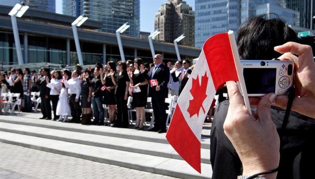 A woman takes a photograph while holding a Canadian flag as a group of 61 new Canadians take the oath of citizenship during a citizenship ceremony held as part of Canada Day celebrations in Vancouver, B.C., on Wednesday July 1, 2009.