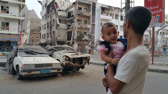 A Yemeni man carrying his daughter looks at a building destroyed during fighting against Houthi fighters in the port city of Aden, Yemen, Sunday, July 19, 2015.