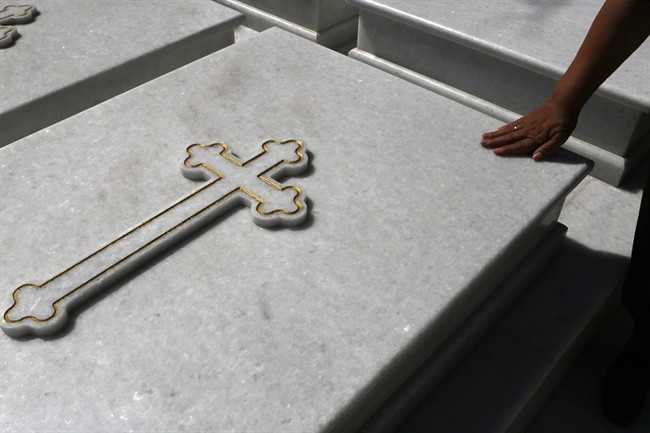 A woman touches a grave at a cemetery in Athens, Friday, July 17, 2015.