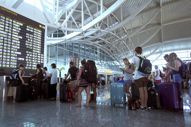 Passengers line up as they checked their flight status at Bali international airport, Indonesia Friday, July 10, 2015. Ash spewing from a volcano on Indonesia's main island of Java has sparked chaos for holidaymakers as airports close and international airlines cancel flights to tourist hotspot Bali, stranding thousands. (AP Photo/Firdia Lisnawati).