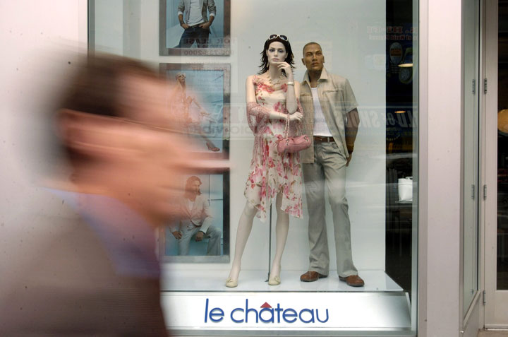 Pedestrians walk past retail clothing displays at a Le Chateau store.