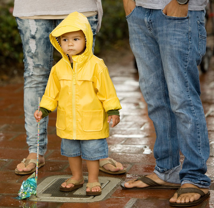Ezekiel Ekinaka, 1, with his parents Aaron and Juliet, wears a raincoat as he experiences rain for the second time in his life, at the San Clemente, Calif. Ocean Festival before the public was urged to evacuate due to lightning on Saturday, July 18, 2015.
