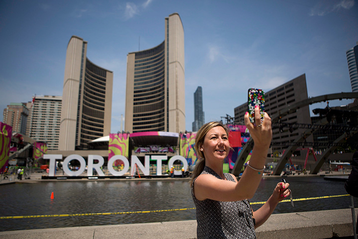 A woman is seen taking a selfie in front of giant letters spelling out Toronto, as workers set up for Pan Am Games public events in Nathan Phillips Square on Wednesday, July 8, 2015.