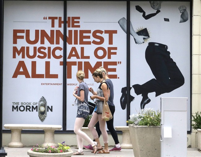 People walk past signs announcing the "Book of Mormon" musical at the Capitol Theatre, Monday, July 27, 2015, in Salt Lake City. The biting satirical musical that mocks Mormons is finally coming to the heart of Mormonlandia, starting a sold-out, two week run on Tuesday, July 28, 2015, at a theater two blocks from the church’s flagship temple and headquarters. (AP Photo/Rick Bowmer).