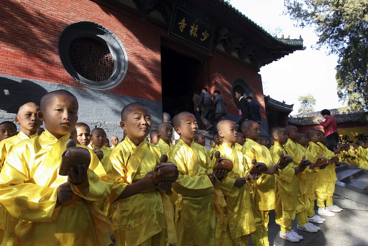 In this Oct. 22, 2012 photo, visitors walk past as young monks offer prayers outside the Shaolin Temple in Dengfeng city in central China's Henan province. (AP Photo) CHINA OUT.
