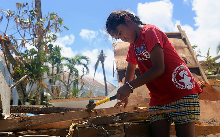A girl helps her parents repair their storm-damaged home by removing nails from plywood on Saturday, Aug. 8, 2015, in Saipan, Northern Mariana Islands.