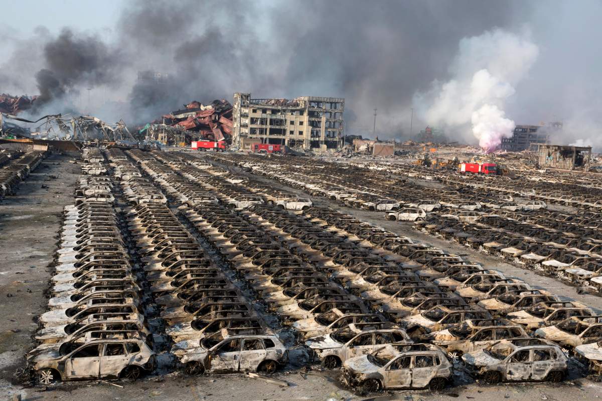 Smoke billows out from the site of an explosion that reduced a parking lot filled with new cars to charred remains at a warehouse in northeastern China’s Tianjin municipality, Thursday, Aug. 13, 2015. Huge explosions in the warehouse district sent up massive fireballs that turned the night sky into day in the Chinese port city of Tianjin, officials and witnesses said Thursday. (AP Photo/Ng Han Guan)