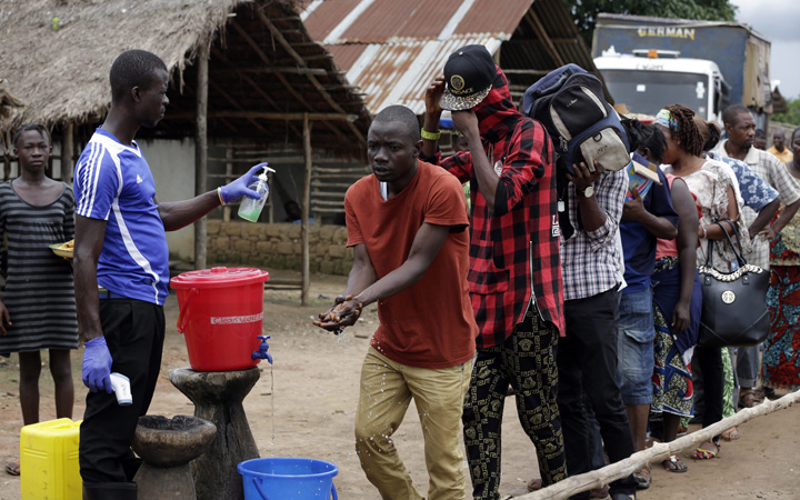 A man takes checks people's temperature and helps to wash their hands as they leave Ebola quarantine, after Sierra Leone President Ernest Bai Koroma cut a tape to release the quarantine in the village of Massessehbeh on the outskirts of Freetown, Sierra Leone on Aug. 14, 2015.