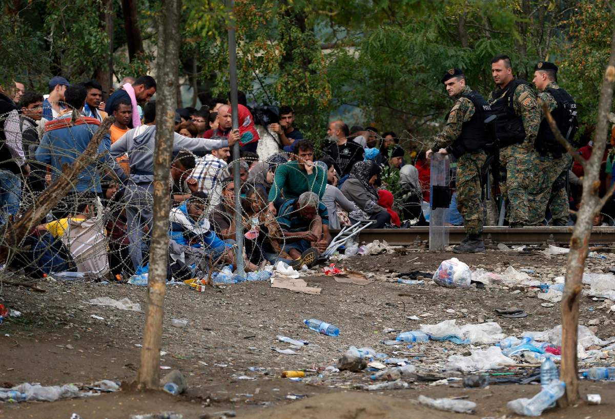 Migrants stand behind the barbed wire set by Macedonian police to stop thousands of migrants entering Macedonia illegally from Greece, near the southern Macedonian town of Gevgelija, Saturday, Aug. 22, 2015. 