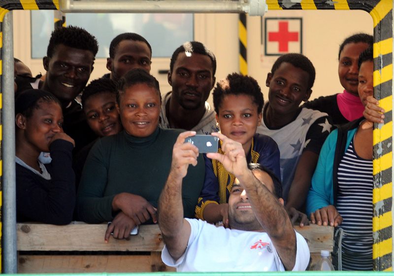A crew member of the MSF (Doctors Without Borders) ship takes a selfie photo with migrants upon their arrival at the Vibo Valentia's harbor, Italy, Sunday, Aug. 23, 2015.