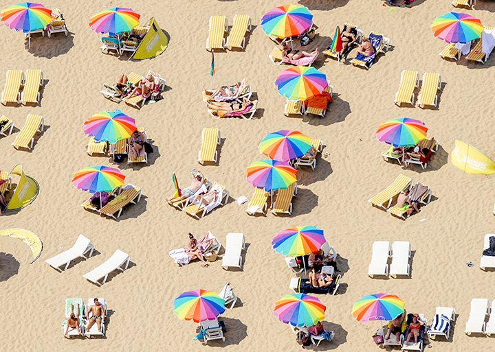 An aerial view shows sunbathers sitting under colorful umbrellas on the beach in Scheveningen, the Netherlands, on July 1, 2015, on a warm summer day. 