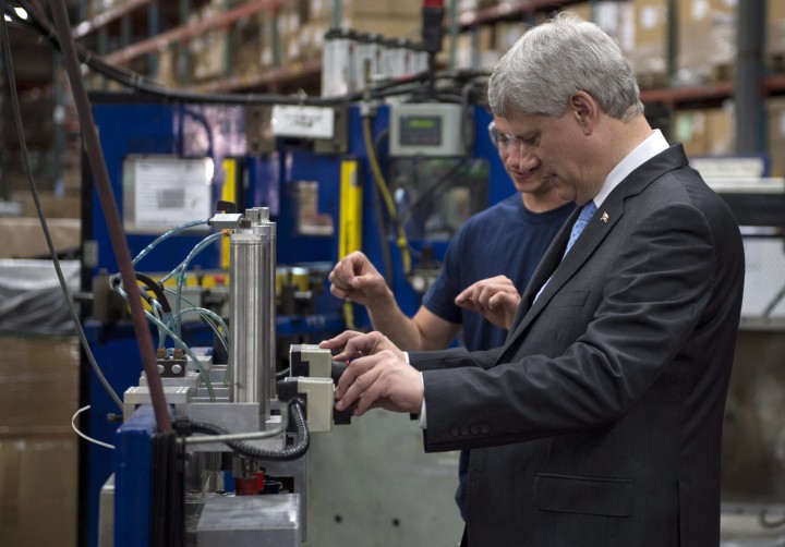 Conservative Leader Stephen Harper gets instructions on how to operate a machine that puts the finishing touch to a radiator while touring a industrial parts manufacture Monday, August 3, 2015 in Laval, Que.
