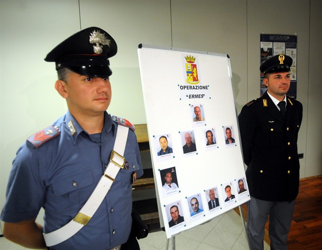 An Italian Carabinieri paramilitary police officer and a police officer stand next to mug shots of 11 men suspected of helping Matteo Messina Denaro during a press conference in Palermo, Italy, Monday, Aug. 3, 2015.