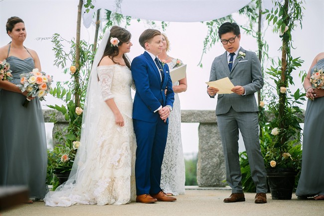 In this Aug. 22, 2015 photo, provided by Lisa Rigby shows Blake Keng, right, reading from Supreme Court Justice Anthony Kennedy’s recent opinion on same-sex marriage during the wedding of Jillian Levine Smith, left, and Emily Smith, center, in Provincetown, Mass. Many couples, both gay and straight, are choosing to include words from the opinion in their ceremonies.