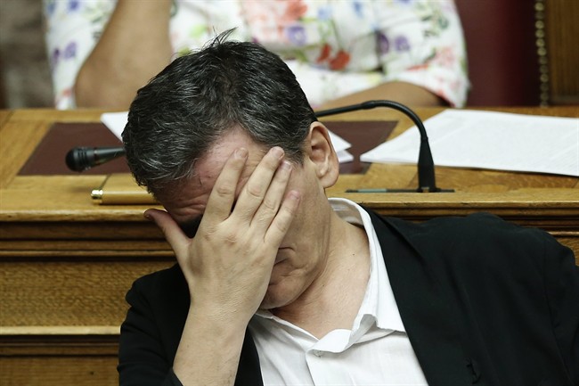 Greek Finance Minister Euclid Tsakalotos covers his face during a parliamentary session in Athens, early Friday, Aug. 14, 2015. The Greek government defended its new bailout program in tumultuous parliamentary sessions as it faced a rebellion in the governing Syriza party ahead of a vote on the deal. (AP Photo/Yannis Liakos).
