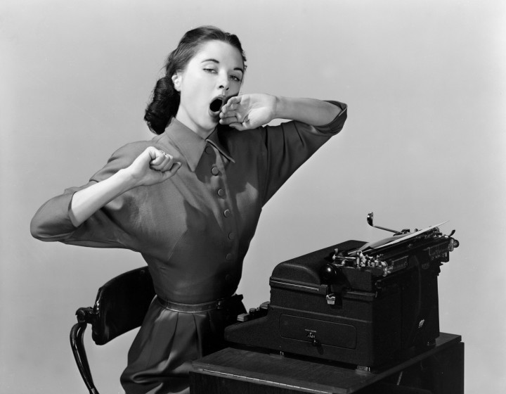 A photograph of a woman sitting yawning at a typewriter, taken by Photographic Advertising Limited in 1950.