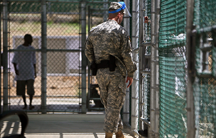 A guard wearing a protective face mask speaks with a detainee through a fence as another paces inside the exercise yard at Camp five detention facility on Guantanamo Bay U.S. Naval Base in Cuba. 