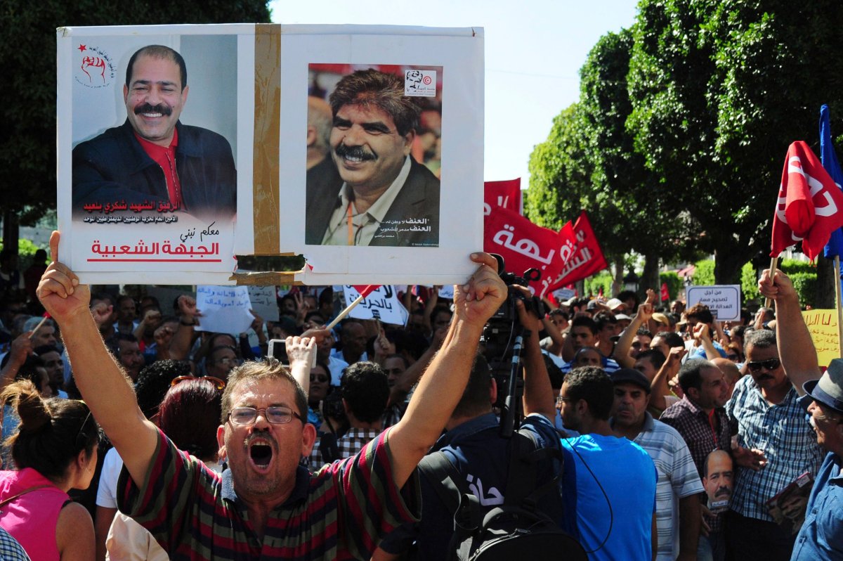 A Tunisian demonstrator holds a poster of slain politicians, lawyer and secular politician Chokri Belaid, left poster, and Mohamed Brahmi, during a march to protest a law offering amnesty for those accused of corruption, in Tunis, Tunisia, Saturday Sept. 12, 2015. 
