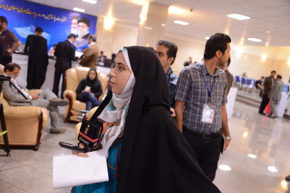 A female correspondent working for HispanTV in a black chador holds a microphone with the TV logo on it while observing the candidates enrolling for presidential election in the registration hall of  the Ministry of Interior on May 10, 2013 in Tehran, Iran. (Photo by Kaveh Kazemi/Getty Images).
