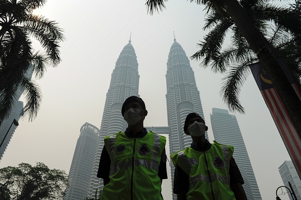 Malaysian policemen wear face masks as Malaysia's iconic Petronas Twin Towers (back) are seen shrouded by haze in Kuala Lumpur on September 11, 2015.