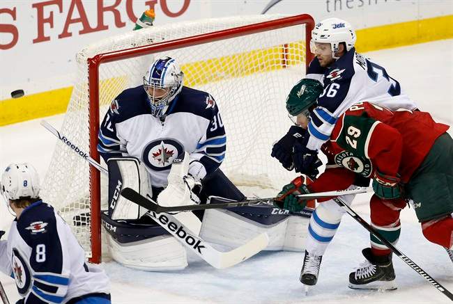 Winnipeg Jets defenseman Joshua Morrissey holds onto Minnesota Wild right wing Jason Pominville as Jets goalie Connor Hellebuyck deflects a shot by Pominville during the third period of an NHL preseason hockey game in St. Paul, Minn.