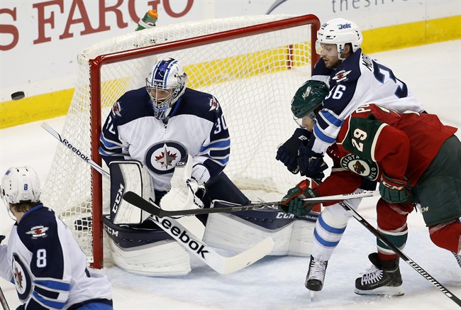 Winnipeg Jets defenseman Joshua Morrissey holds onto Minnesota Wild right wing Jason Pominville as Jets goalie Connor Hellebuyck deflects a shot by Pominville during the third period of an NHL preseason hockey game in St. Paul, Minn.