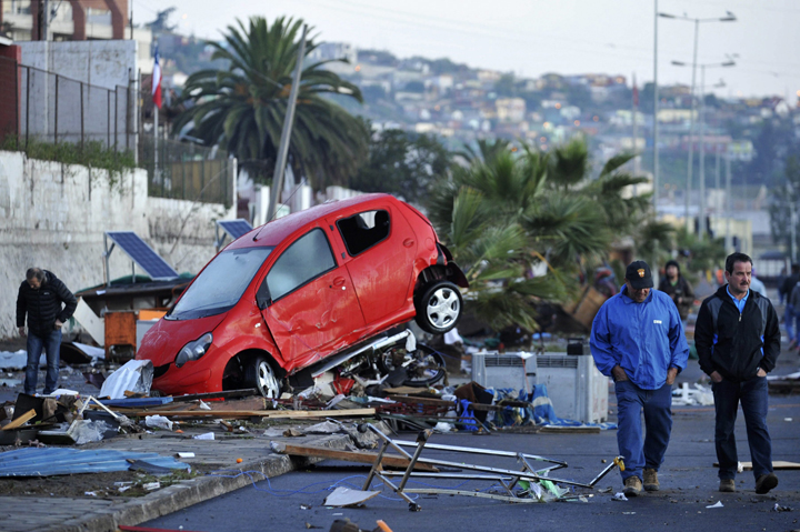 Chileans pass a wrecked car pushed by strong waves, after a magnitude 8.4 Richter scale earthquake, in Coquimbo, Chile, 17 September 2015.