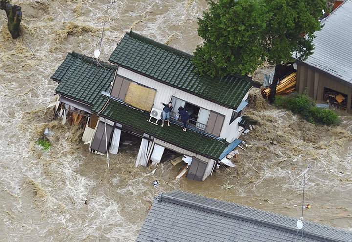 A person inside a house waves to a helicopter as the house is submerged in water flooded from a river in Joso, Ibaraki prefecture, northeast of Tokyo Thursday, Sept. 10, 2015.