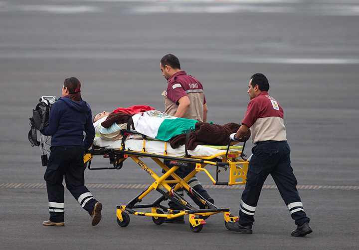 A man wounded in an attack by the Egyptian army while traveling in Egypt, is draped in a Mexican flag as he's transferred from the return flight to a waiting helicopter at the presidential hangar of Benito Juarez International Airport in Mexico City, Friday, Sept. 18, 2015.  