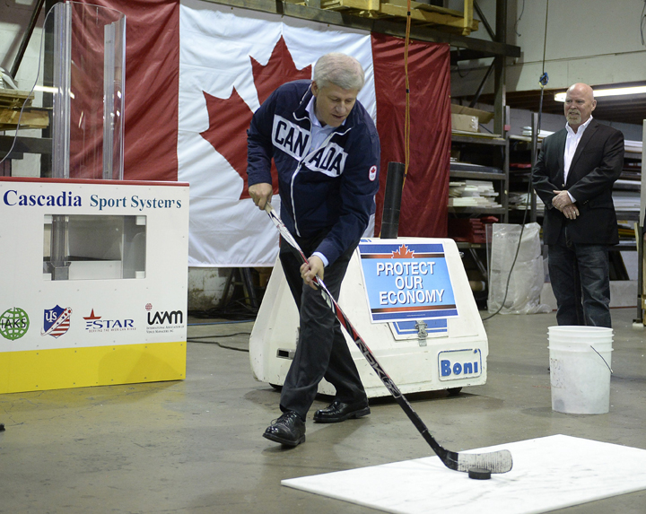 Conservative Leader Stephen Harper takes a shot during a campaign stop at a company that makes hockey rink boards in Port Moody, B.C.,  Tuesday, Sept.15,.
